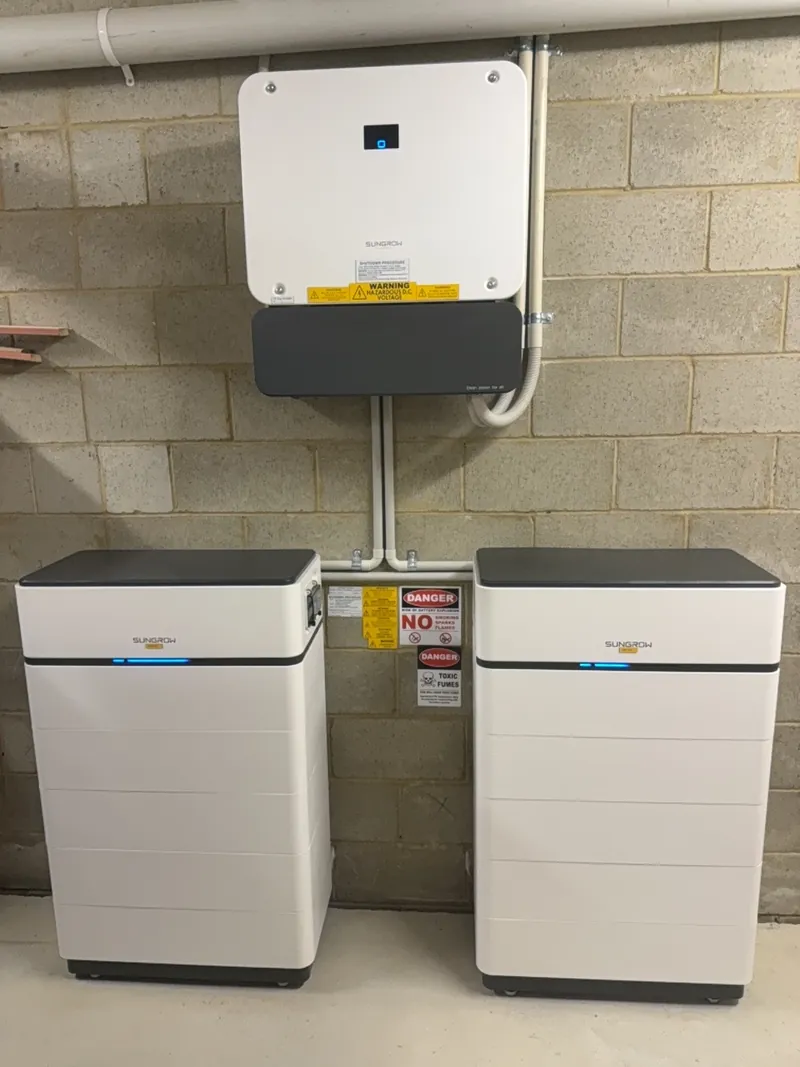 Two white home battery units installed below a solar inverter on a block wall