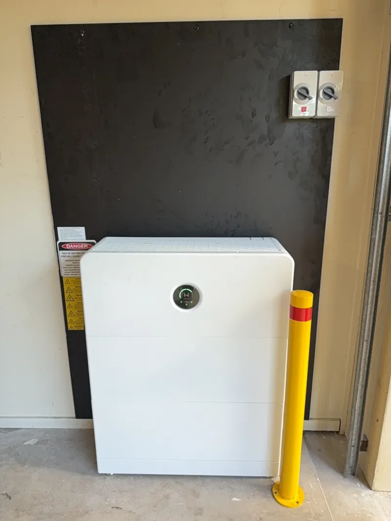 White home battery cabinet in a garage protected by a yellow safety bollard