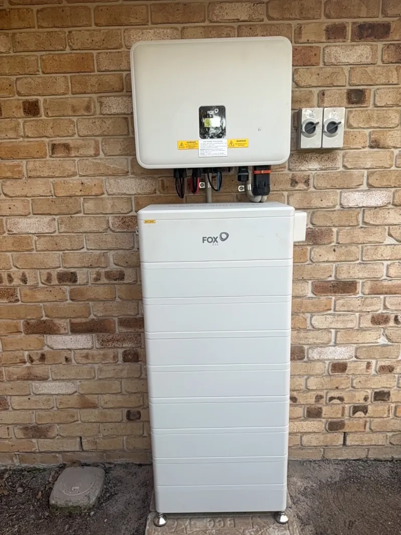 Stacked home battery and solar inverter mounted on an exterior brick wall