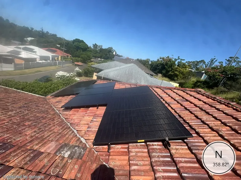 Black solar panels on a terracotta tile roof overlooking a Brisbane valley