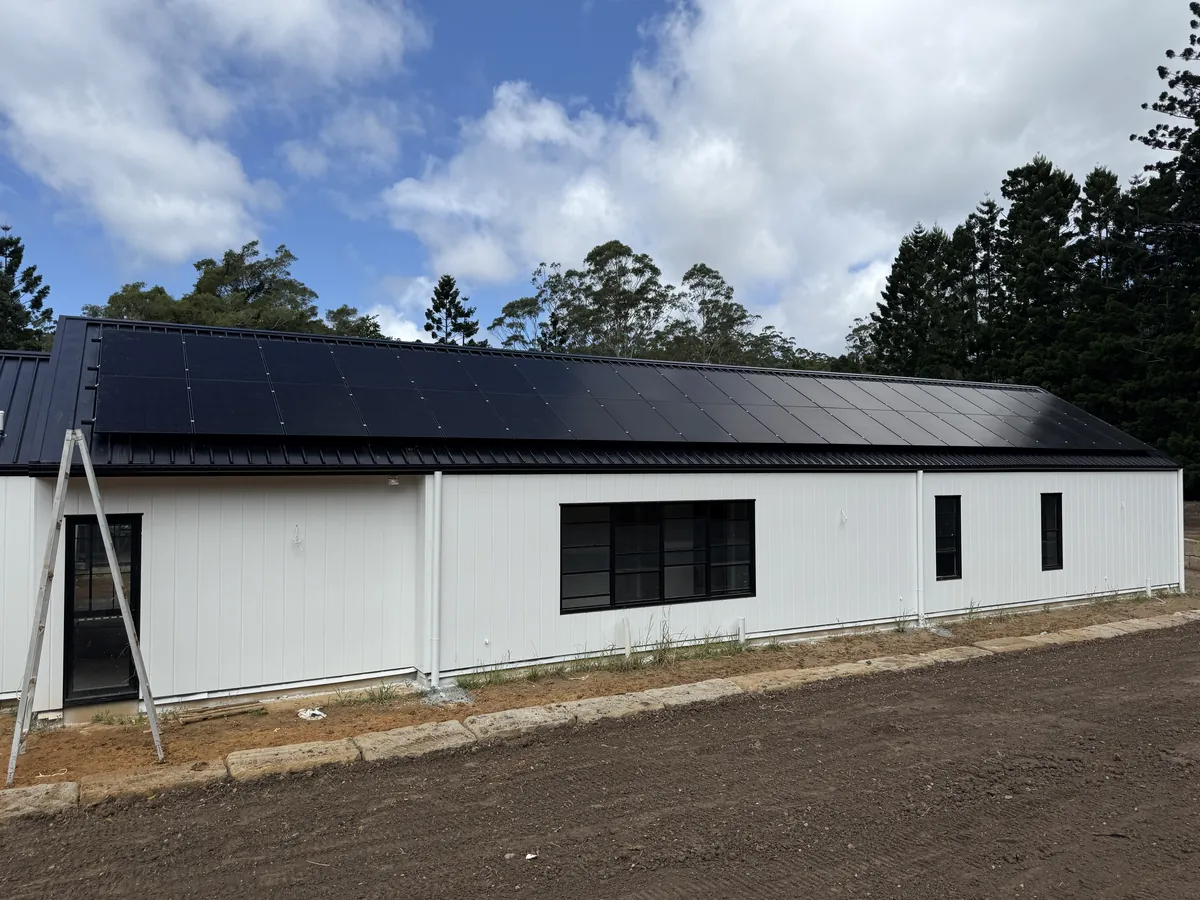 Large black solar array covering the roof of a white rural shed under blue sky